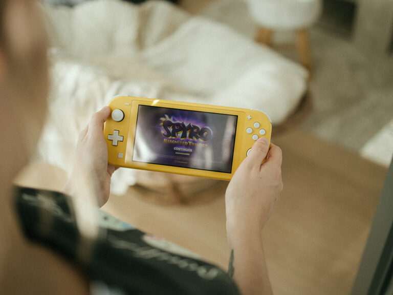 Iemand houdt gele spelcomputer vast en speelt het spel Spyro. Opletten dat de game-activiteit niet de overhand gaat nemen in je leven.