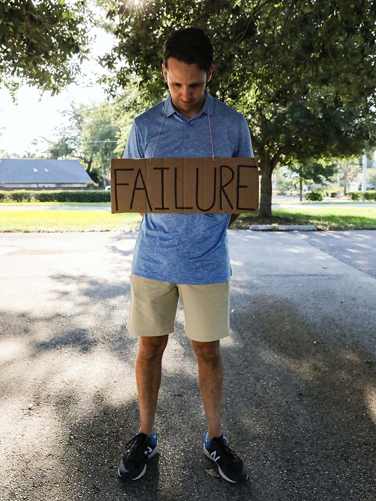 Man heeft bord met het woord 'failure' om zijn nek als symbool voor het negatieve zelfbeeld bij verslaving.